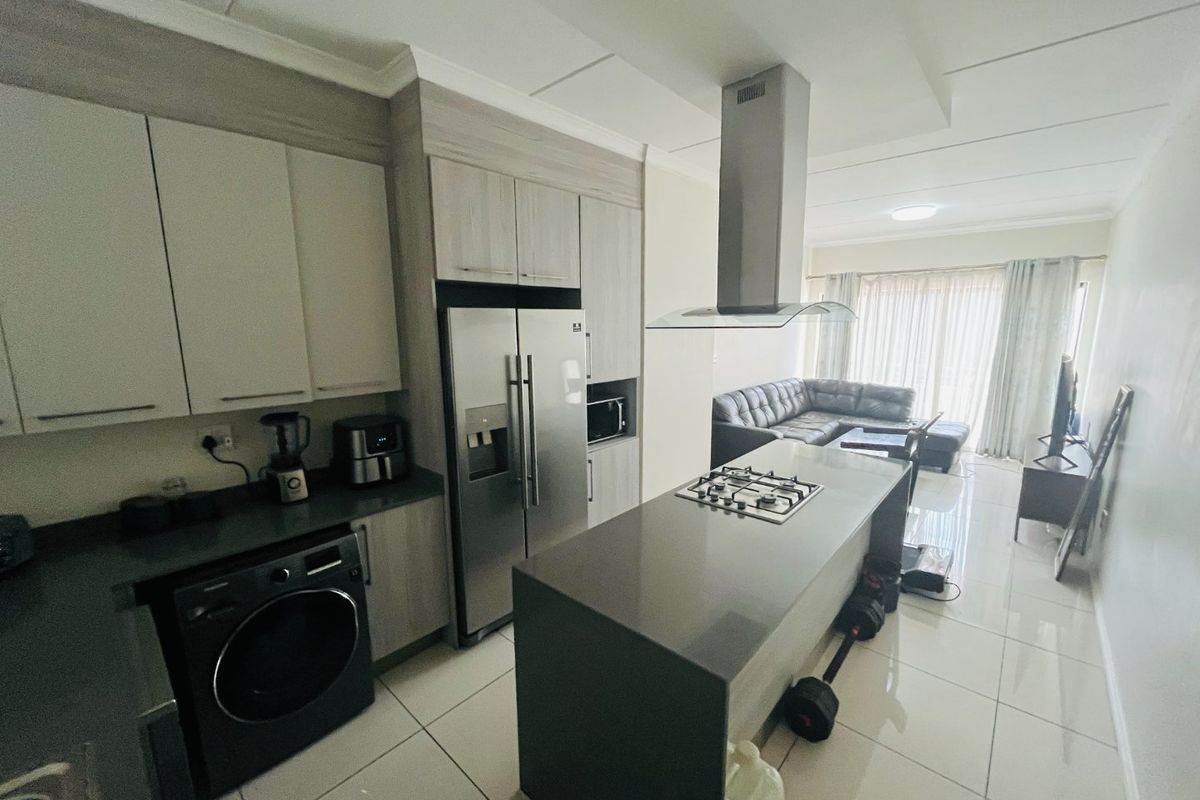 Modern open-plan kitchen and living area featuring sleek cabinetry, stone countertops, a central island with a gas hob, and polished tiled flooring throughout.