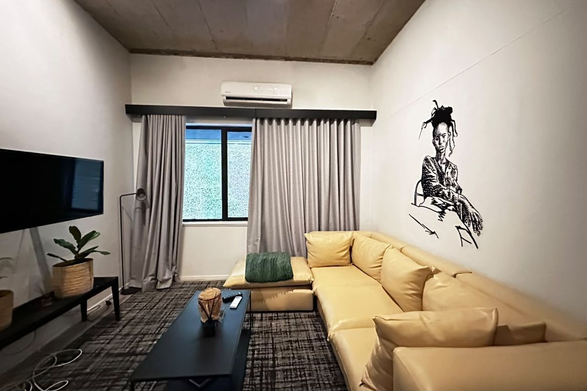 A modern living room featuring an exposed concrete ceiling, split-system air conditioning, and large window with floor-to-ceiling curtains.