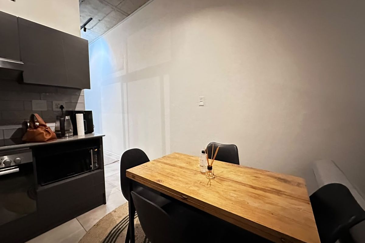 An open-plan kitchen and dining area featuring modern dark cabinetry, built-in appliances, and an exposed concrete ceiling with tiled flooring.