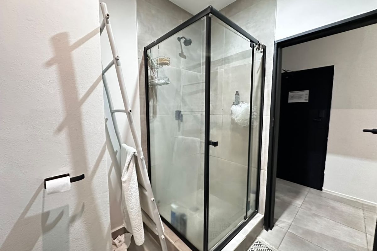 A modern bathroom featuring a glass-enclosed shower with black framing and neutral wall tiling.