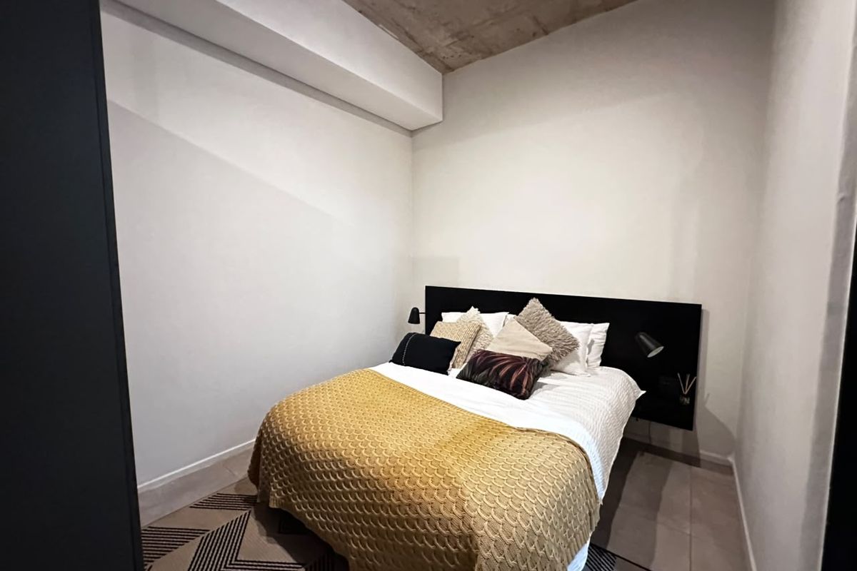 A modern bedroom featuring an exposed concrete ceiling and a sleek, built-in headboard design.