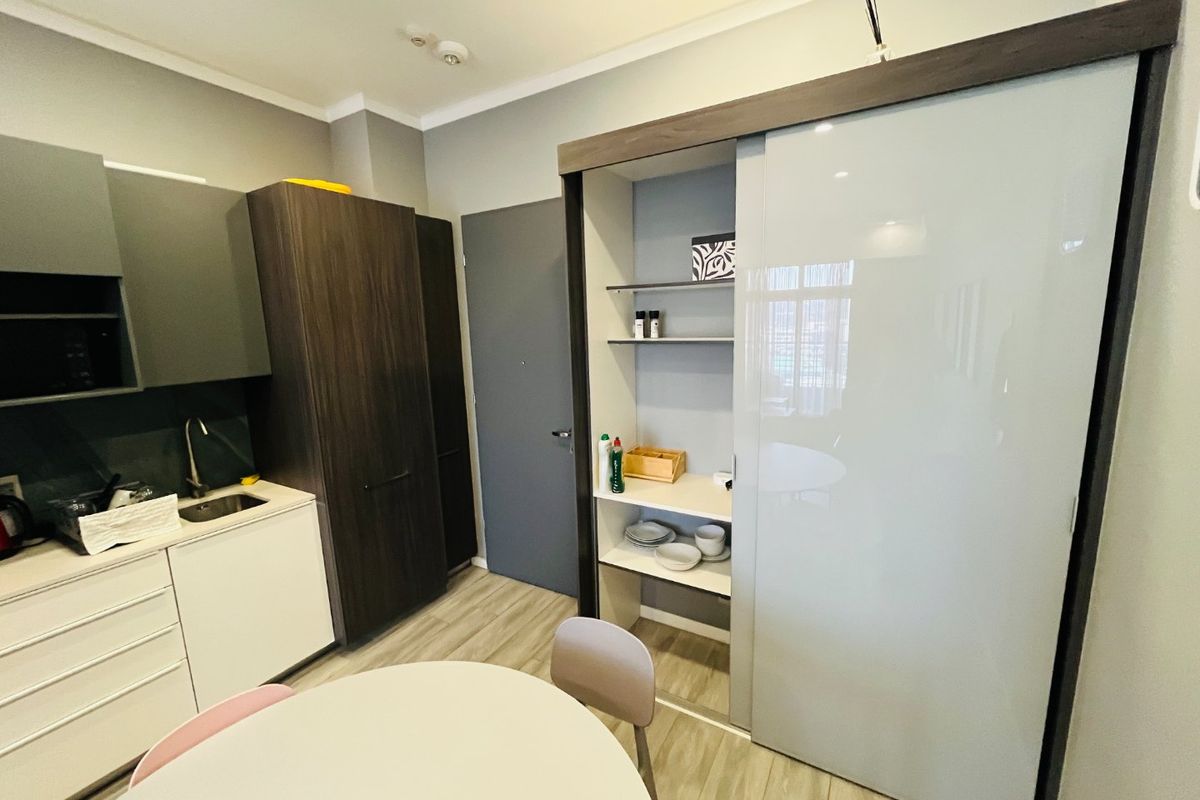 Compact modern kitchen featuring sleek dark and white cabinetry, integrated pantry storage, and durable laminate flooring in a functional apartment layout.