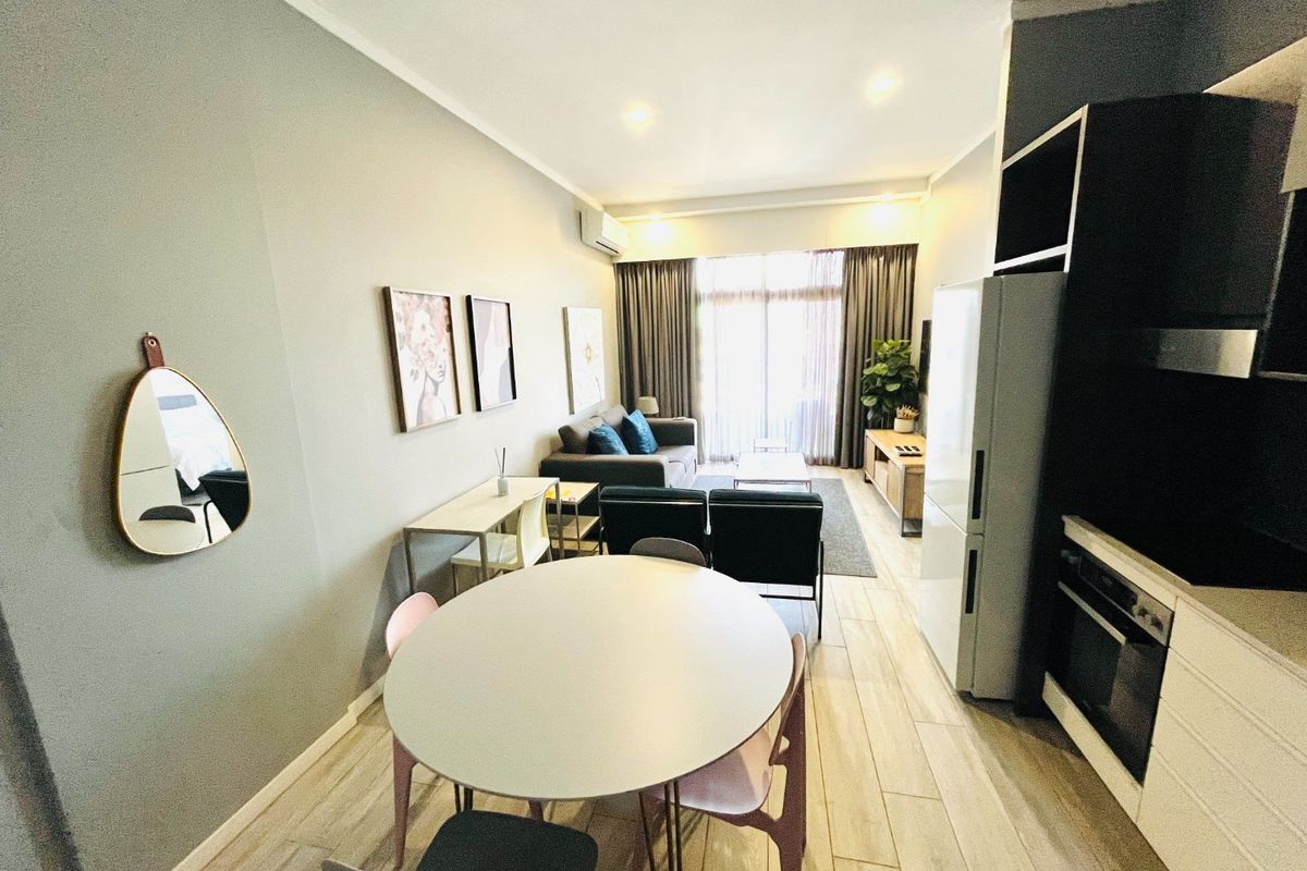 Modern open-plan living area featuring a compact kitchen with built-in oven, tiled flooring, and direct access to a balcony through sliding glass doors.