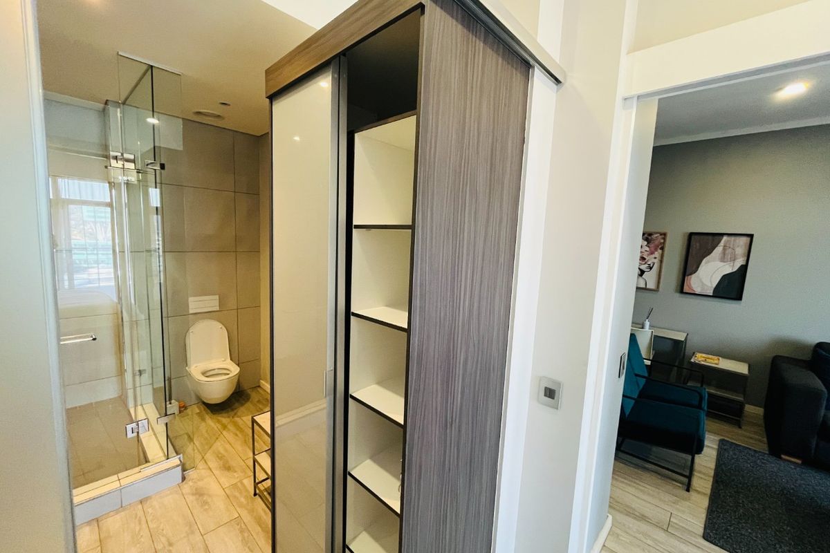 Modern bathroom featuring a glass-enclosed shower, wall-hung toilet, and integrated shelving unit, with neutral tiling throughout.