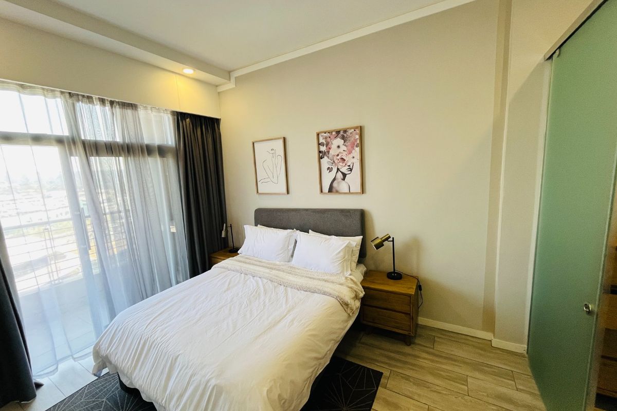 A well-maintained bedroom featuring wood-look tile flooring, recessed lighting, and a sliding glass door providing access to a private balcony.