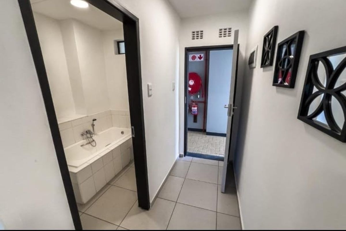 A clean hallway with tiled flooring leading to a bathroom and an exterior exit point featuring a fire extinguisher.