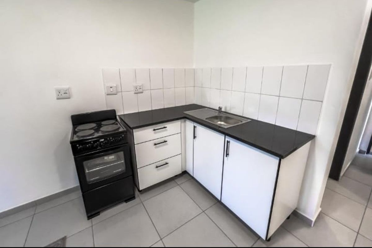 Compact kitchen featuring white cabinetry, black granite countertops, a stainless steel sink, tiled backsplash, and a freestanding electric stove.