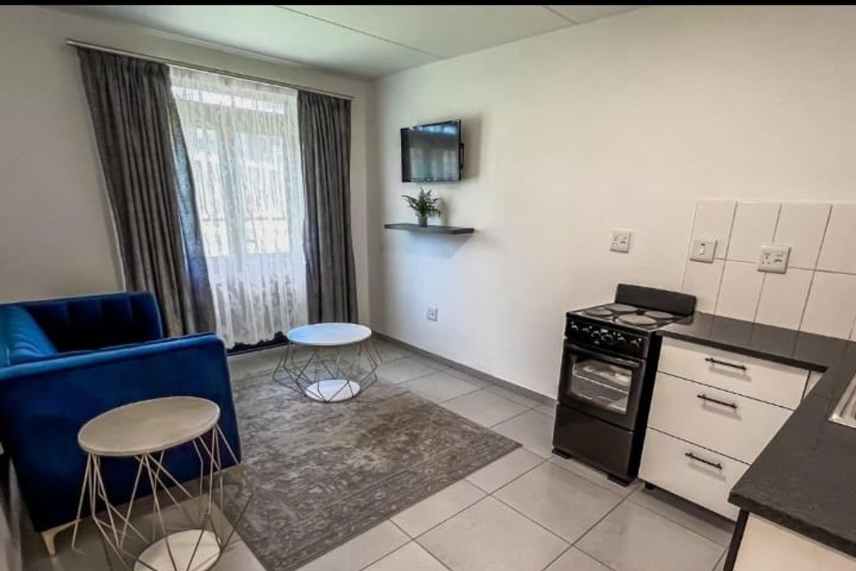 Compact open-plan living area featuring a kitchenette with a freestanding stove, tiled flooring, and neutral finishes, suitable for efficient apartment living.