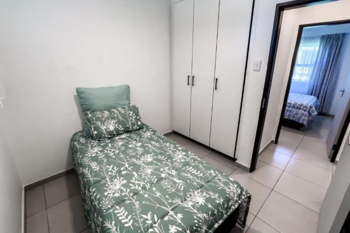 A compact bedroom featuring neutral tiled flooring and a white built-in wardrobe, with a view into an adjacent room.