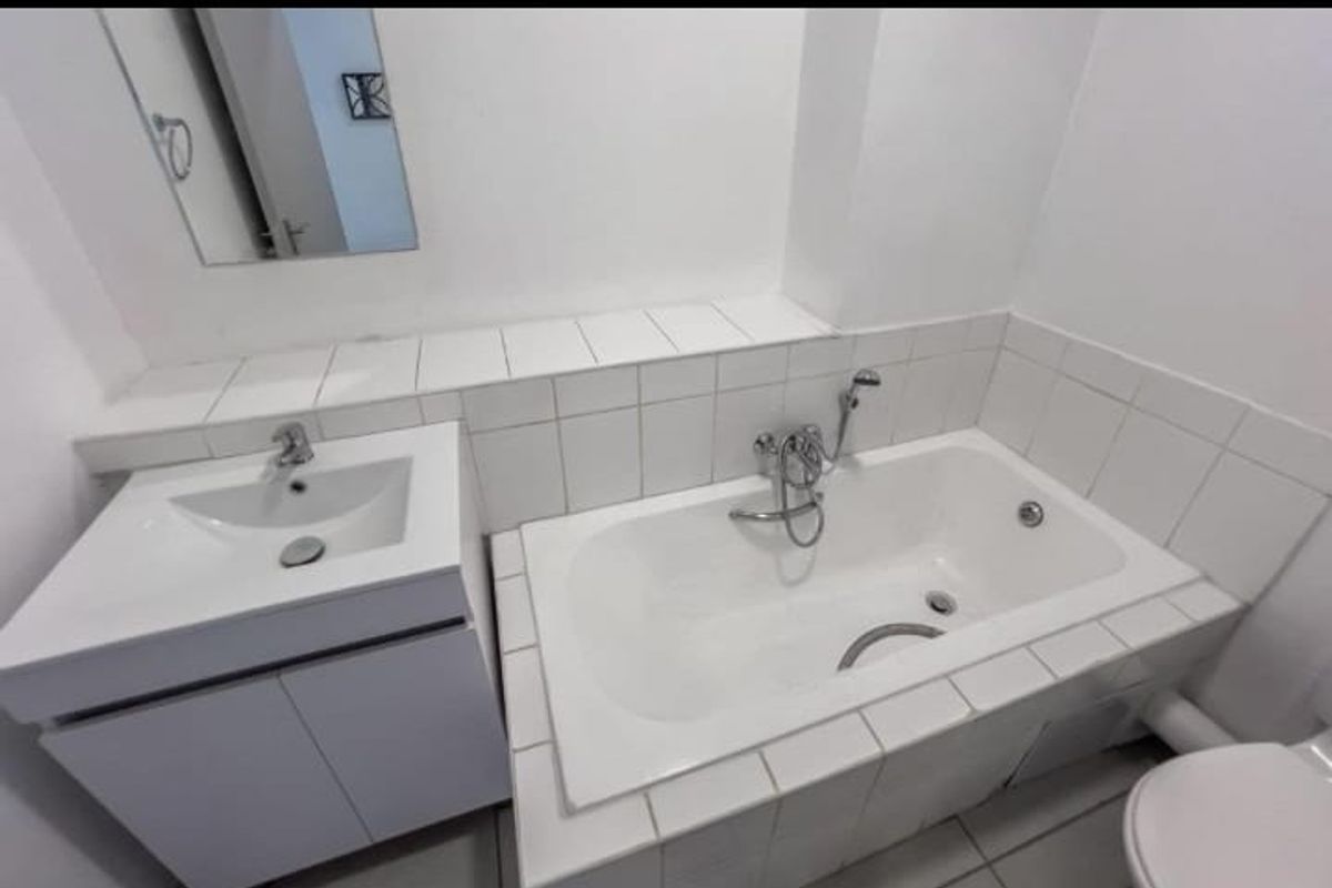 A clean, functional bathroom featuring a built-in vanity, tiled bathtub with handheld shower mixer, and a wall-mounted mirror.