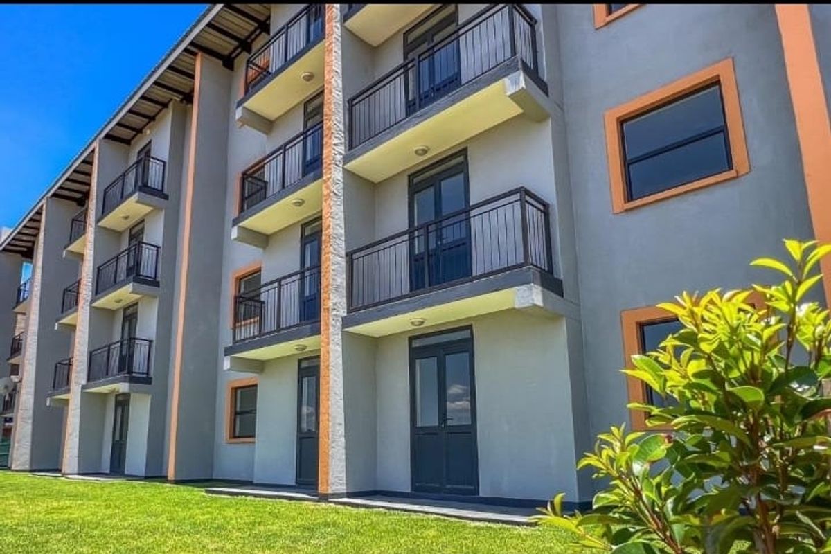 A modern multi-story apartment building exterior featuring stacked balconies with metal railings and well-maintained surrounding lawn areas.