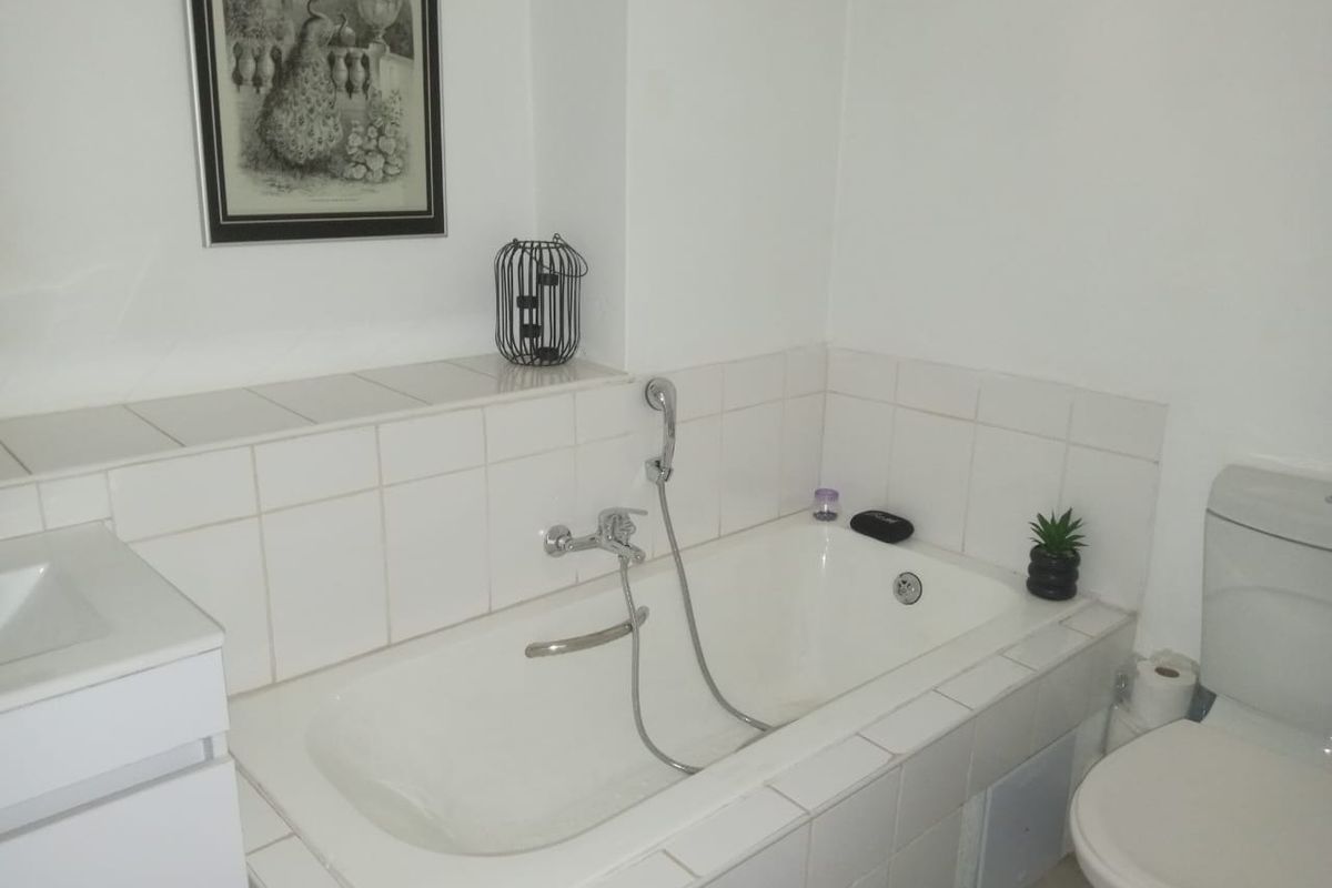A functional bathroom featuring a built-in bathtub with a handheld shower attachment, a toilet, and a vanity basin with white tiled finishes.