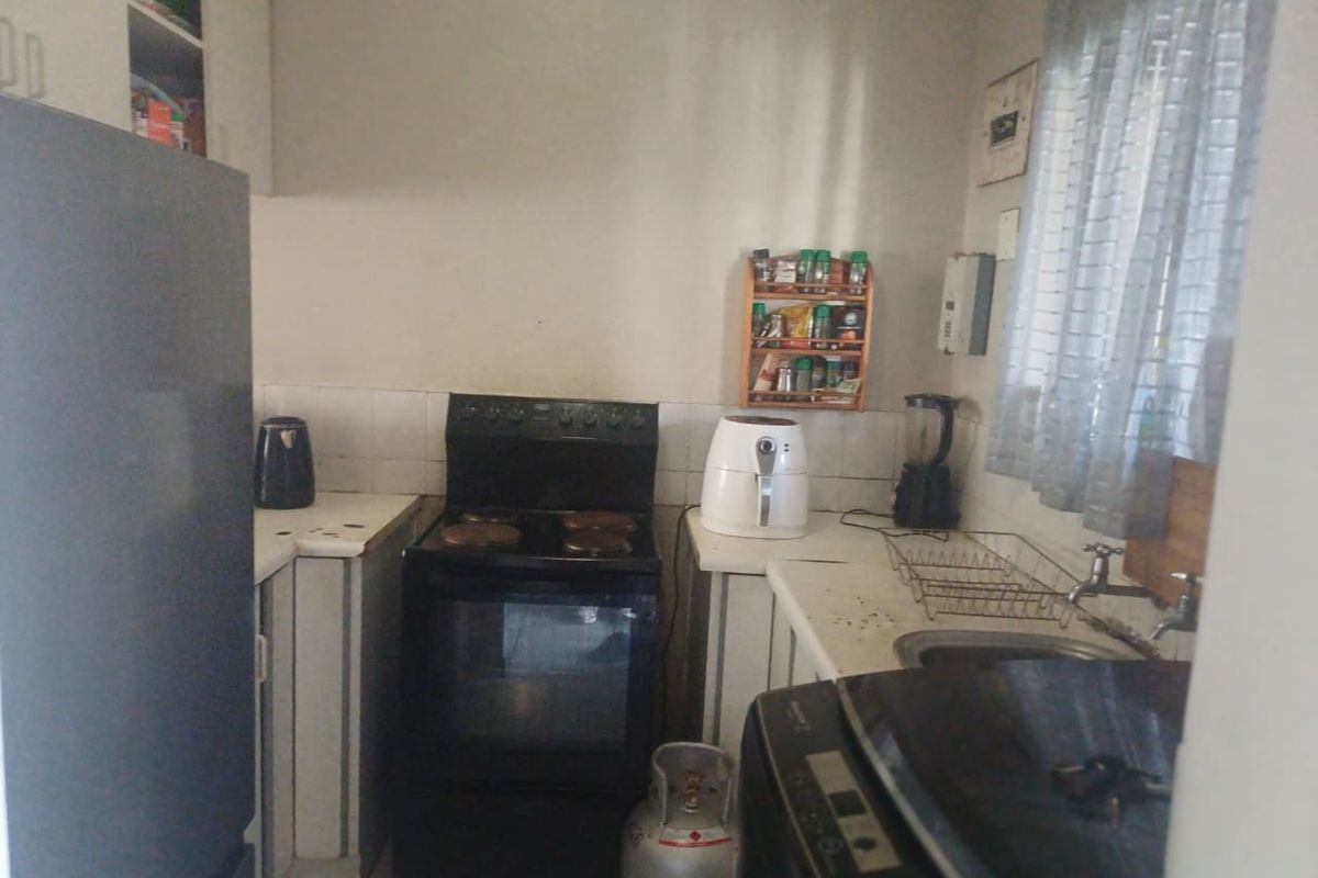 A compact kitchen featuring basic cabinetry, a freestanding stove, and a stainless steel sink with tiled splashback.