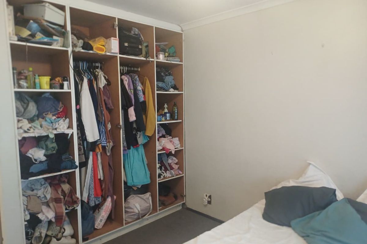 A bedroom featuring a large, multi-section built-in wardrobe with open shelving and hanging space.