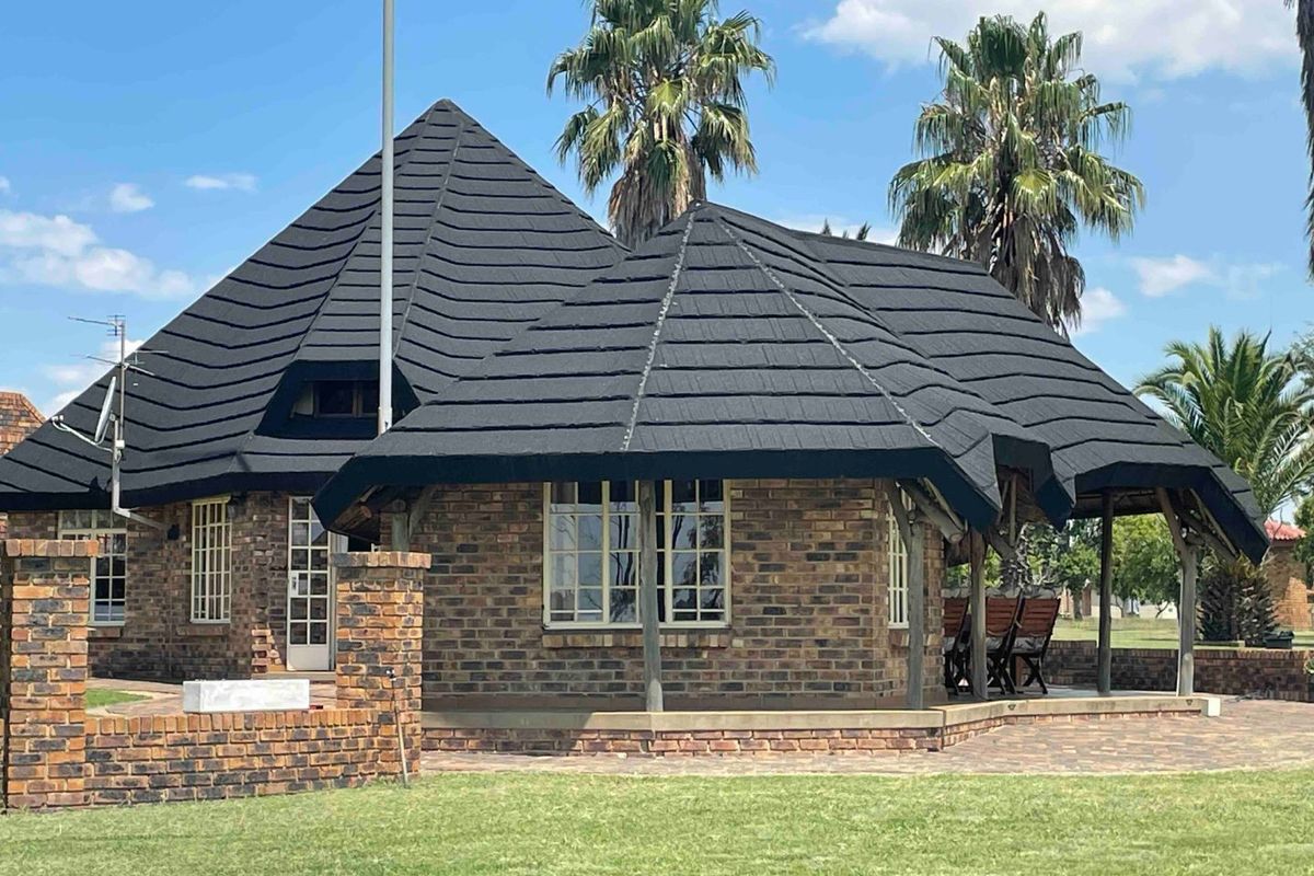 Rear view of a face brick house featuring a distinctive tiled roof, covered patio area with timber supports, and a well-maintained lawn.