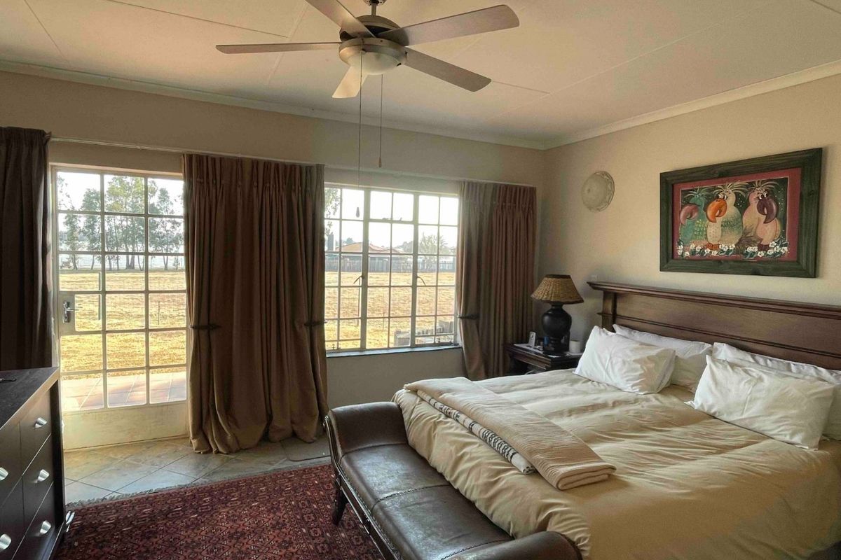Spacious bedroom featuring tiled flooring, a ceiling fan, and large windows with direct access to the exterior through a glass-paneled door.