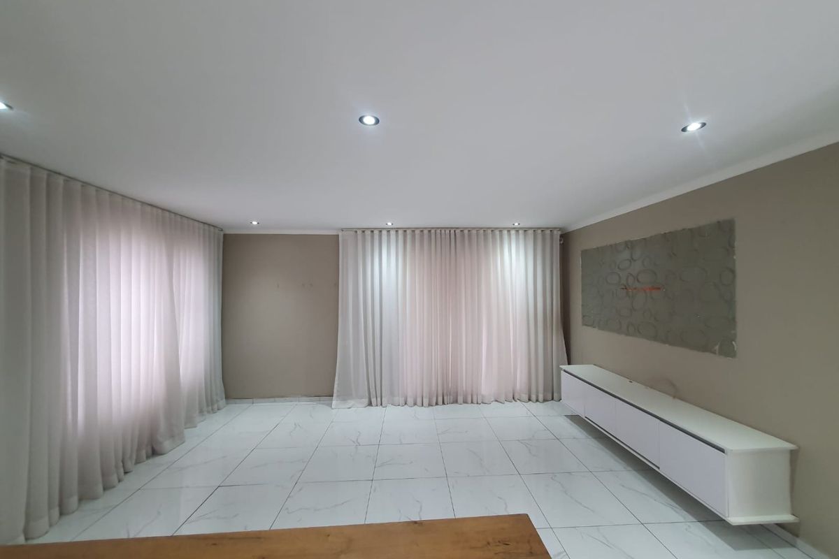 A bright and spacious living room featuring modern marble-look floor tiles, recessed downlighting, and elegant floor-to-ceiling curtains.