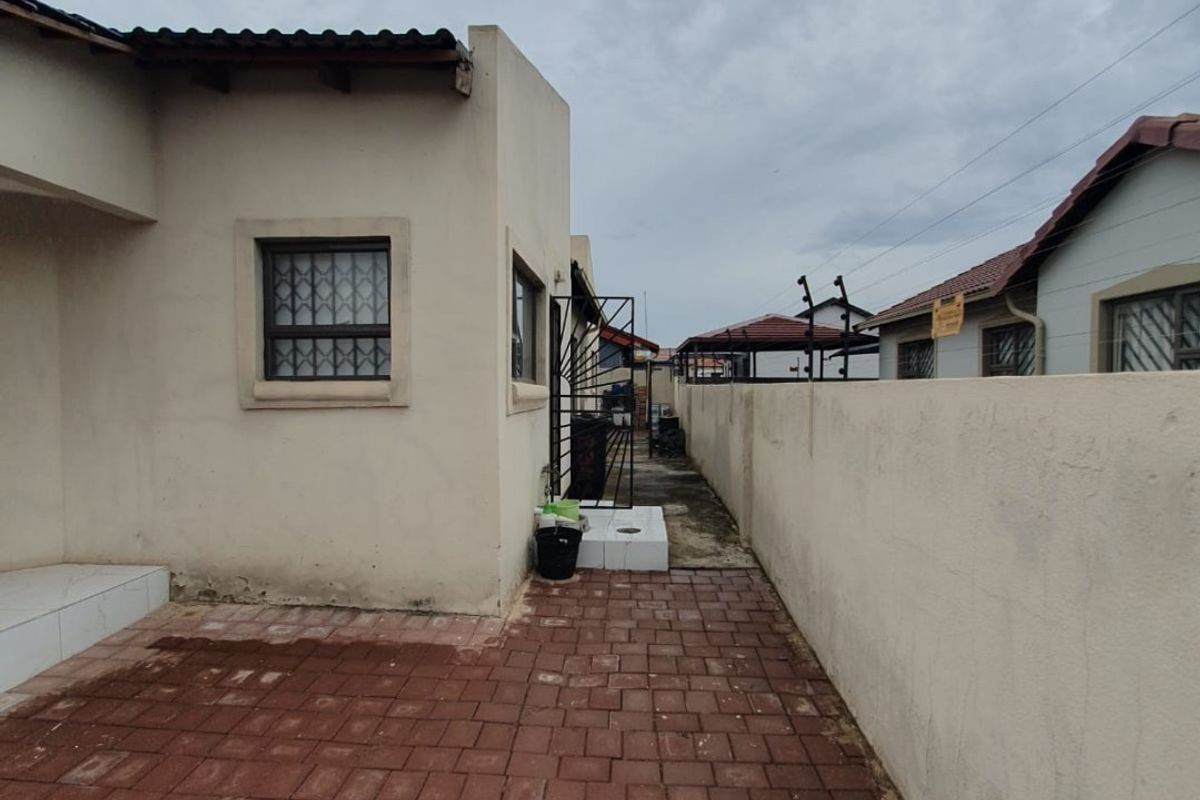 A side exterior view of the property featuring a paved walkway, boundary wall with security spikes, and a metal security gate.