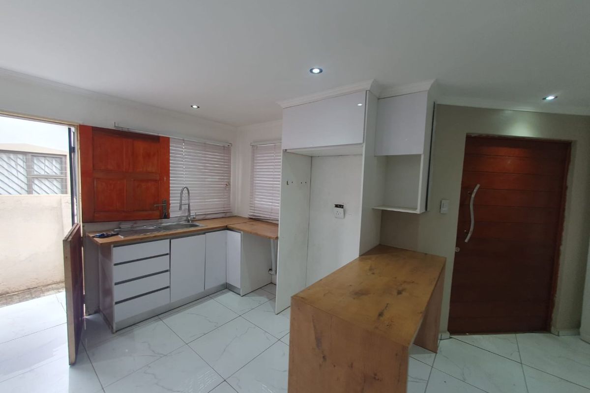 A compact kitchen featuring white cabinetry, wooden countertops, a stainless steel sink, and tiled flooring, currently vacant and ready for final finishing touches.