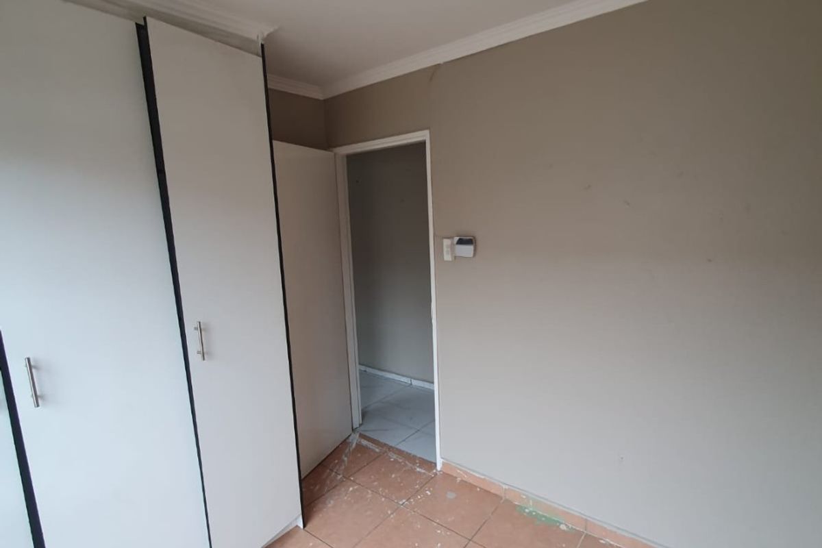 An empty bedroom featuring built-in cupboards, tiled flooring, and neutral wall tones, requiring minor cosmetic touch-ups to restore its finish.