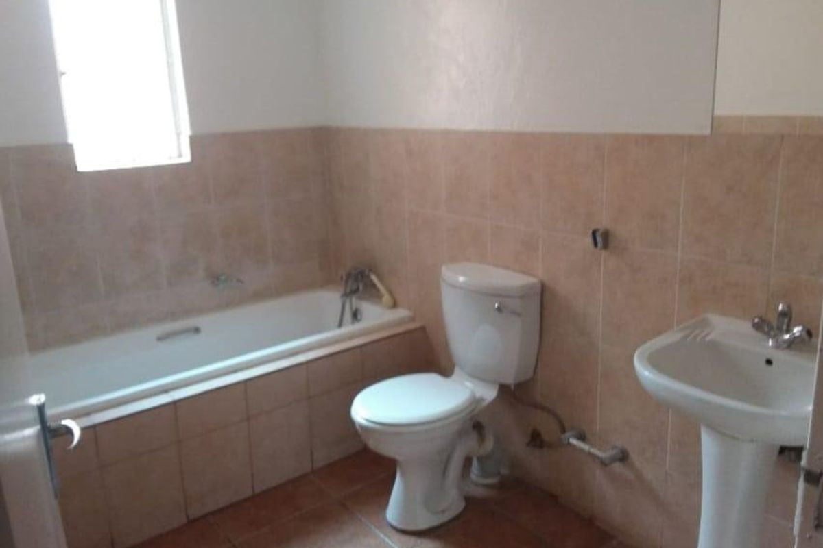 A functional bathroom featuring a bathtub, pedestal basin, and toilet with neutral wall and floor tiling.