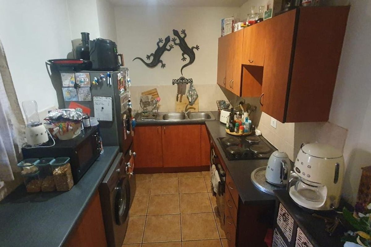 A functional galley-style kitchen featuring laminate cabinetry, dark countertops, a double bowl sink, and an integrated electric hob with oven.
