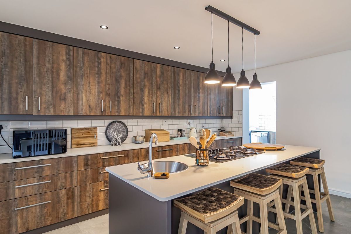 Modern kitchen featuring wood-grain cabinetry, a central island with a gas cooktop, stone countertops, and stylish pendant lighting.