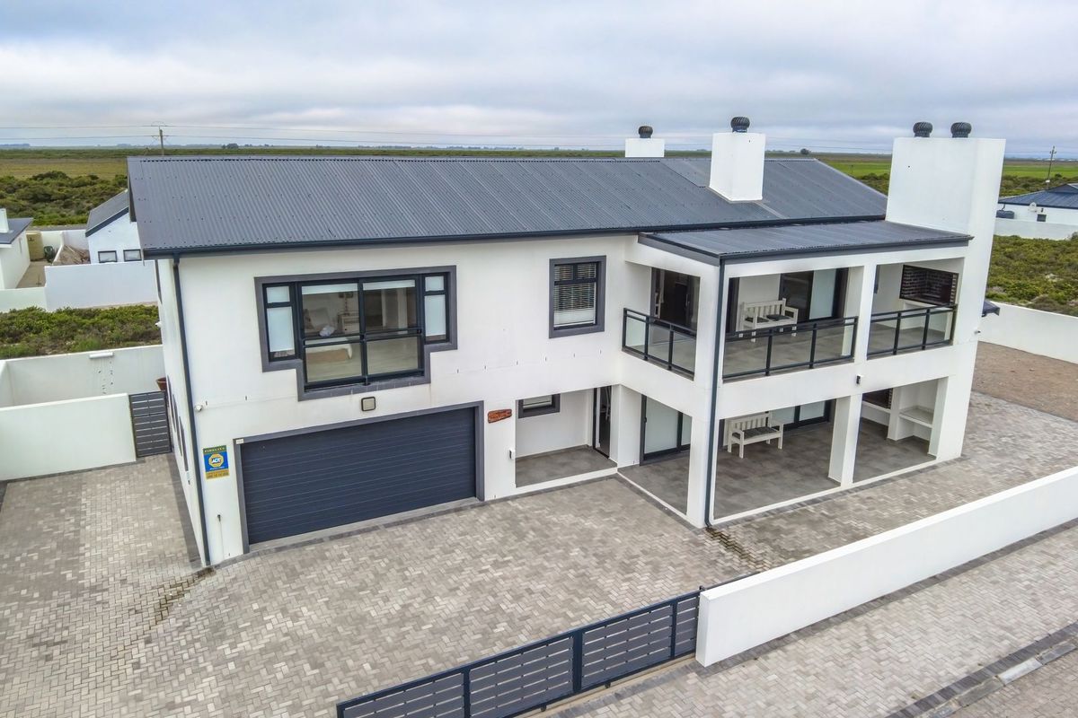 Aerial view of a modern two-story house featuring a paved driveway, double garage, and upper-level balcony with glass balustrades.