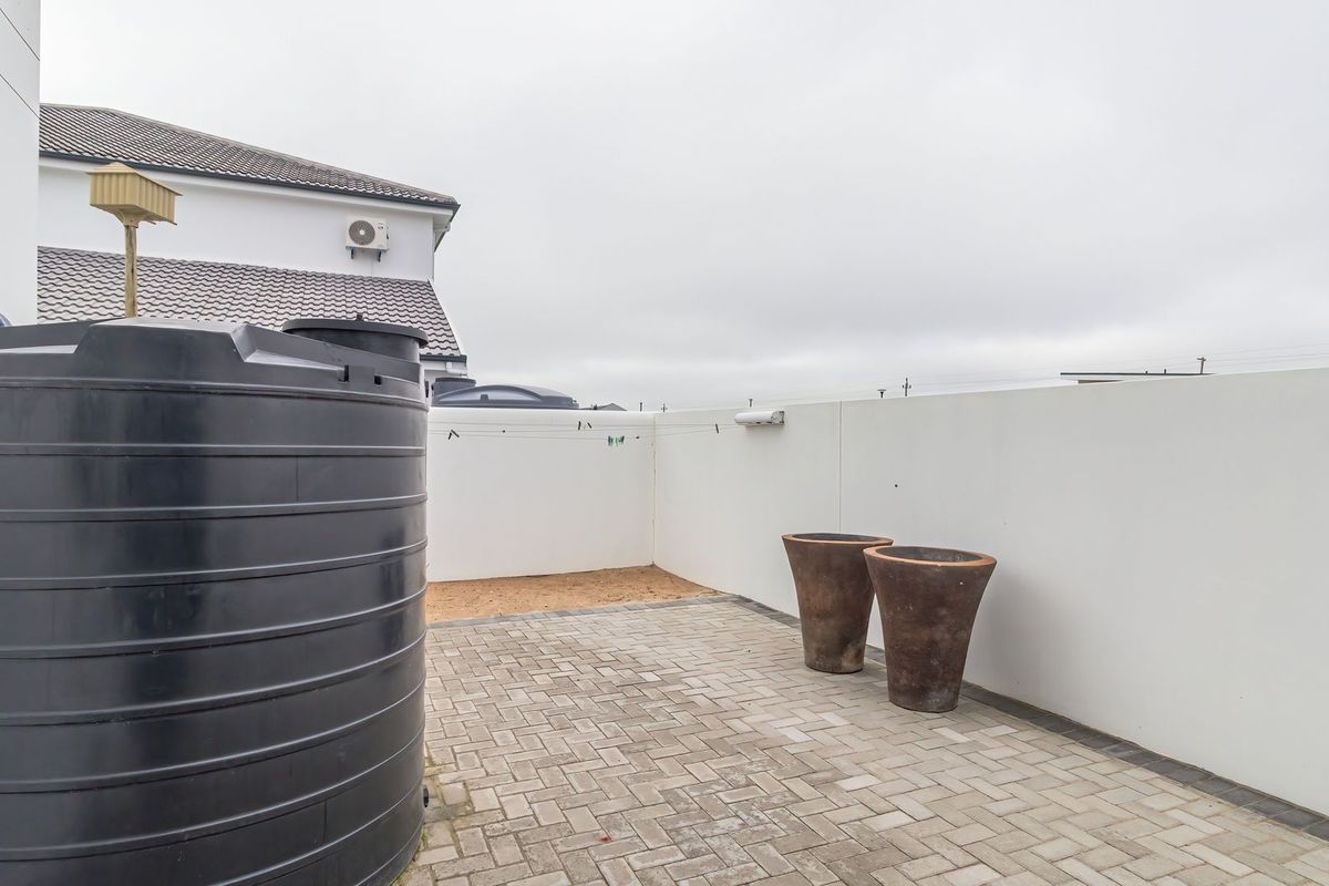 A paved rear courtyard area featuring a large water storage tank, boundary walls, and an exterior air conditioning unit.