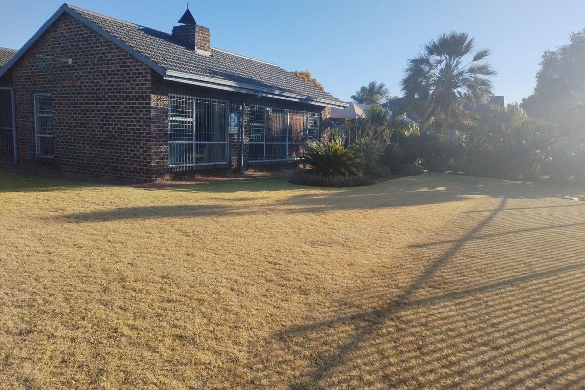 A view of the rear brick facade of the house, featuring a tiled roof, chimney, and a spacious garden area.
