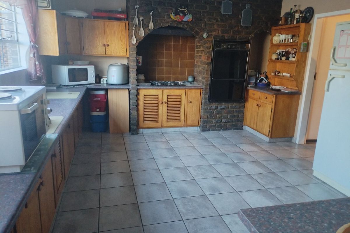 A dated kitchen featuring a prominent brick feature wall, built-in wooden cabinetry, integrated oven, gas hob, and tiled flooring.
