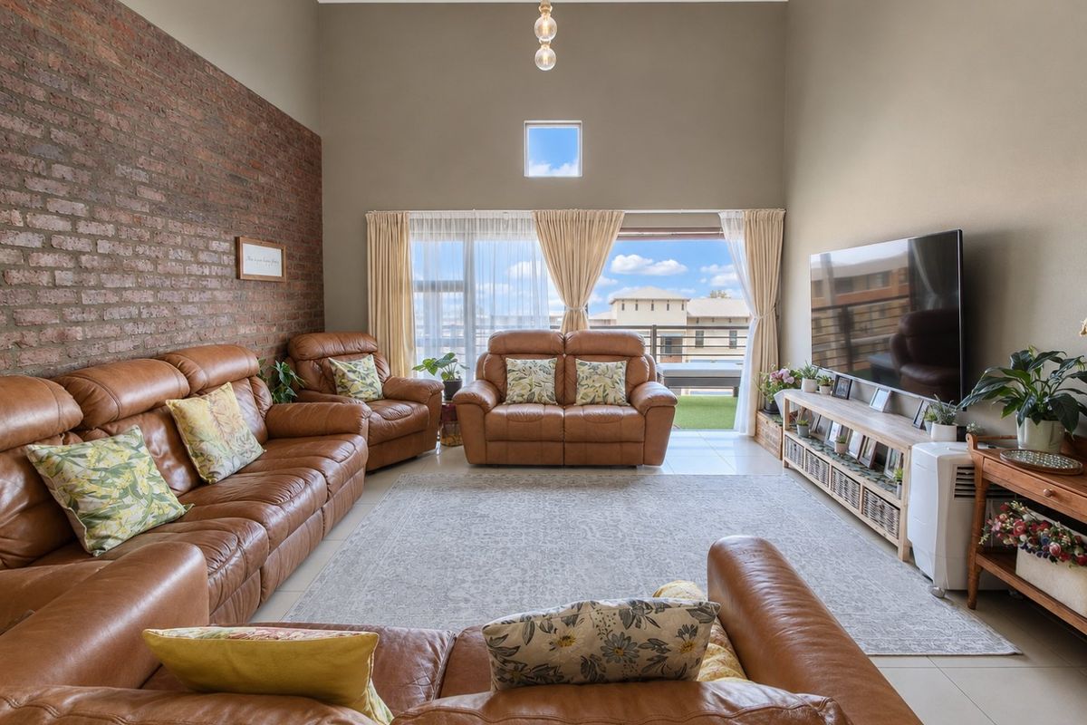 Spacious living room featuring a striking exposed brick wall, high vaulted ceilings, and large sliding doors leading to a balcony with natural light.