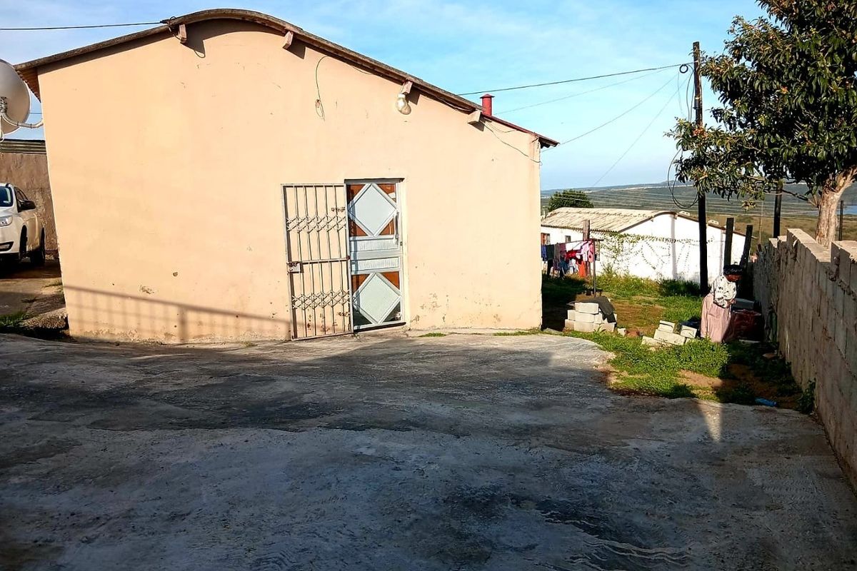 Rear exterior view of the property featuring a concrete driveway, security gate, and boundary wall with visible wear on the building facade.