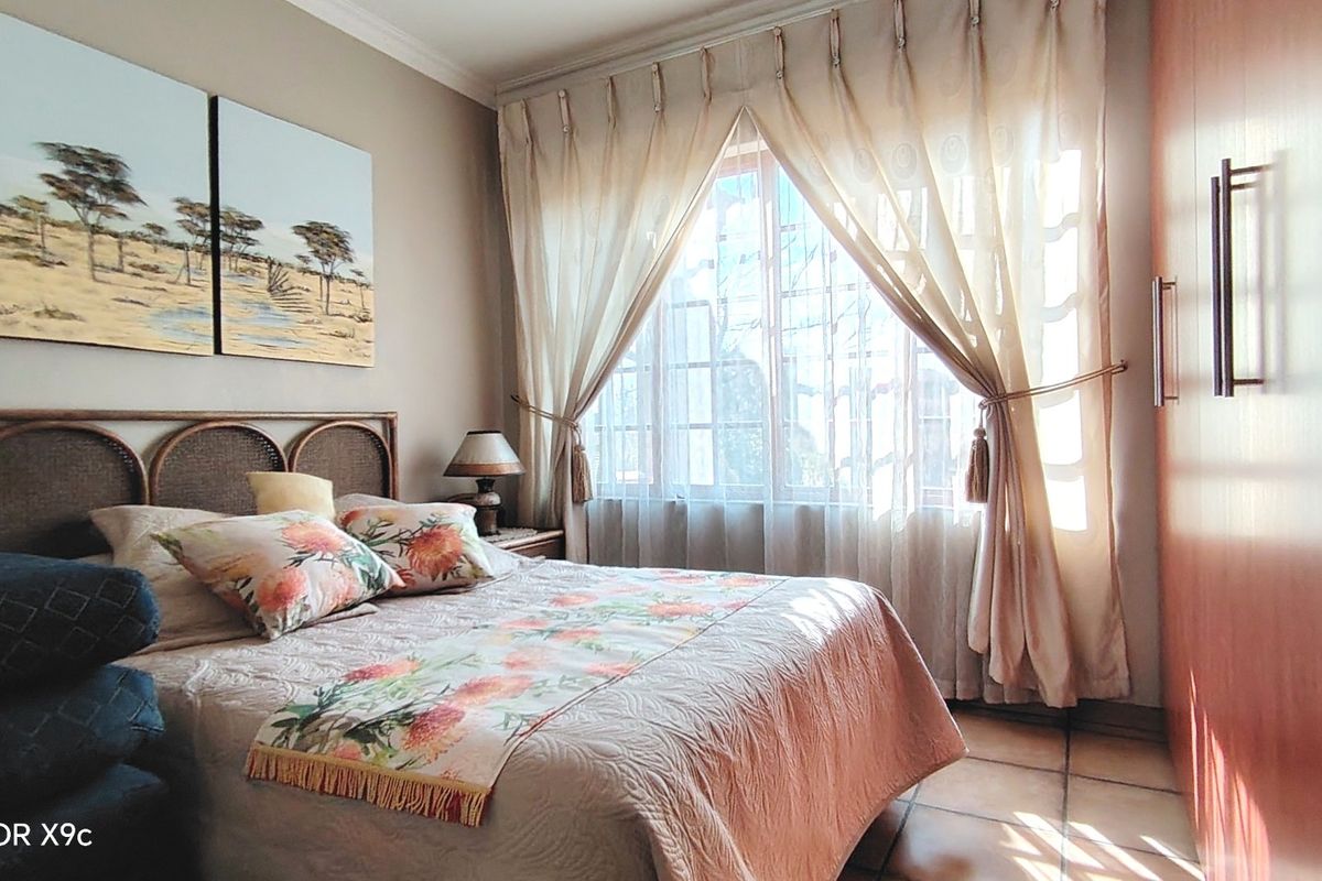 A cozy bedroom featuring tiled flooring, a built-in wardrobe, and a window with security bars, providing a comfortable and functional living space.