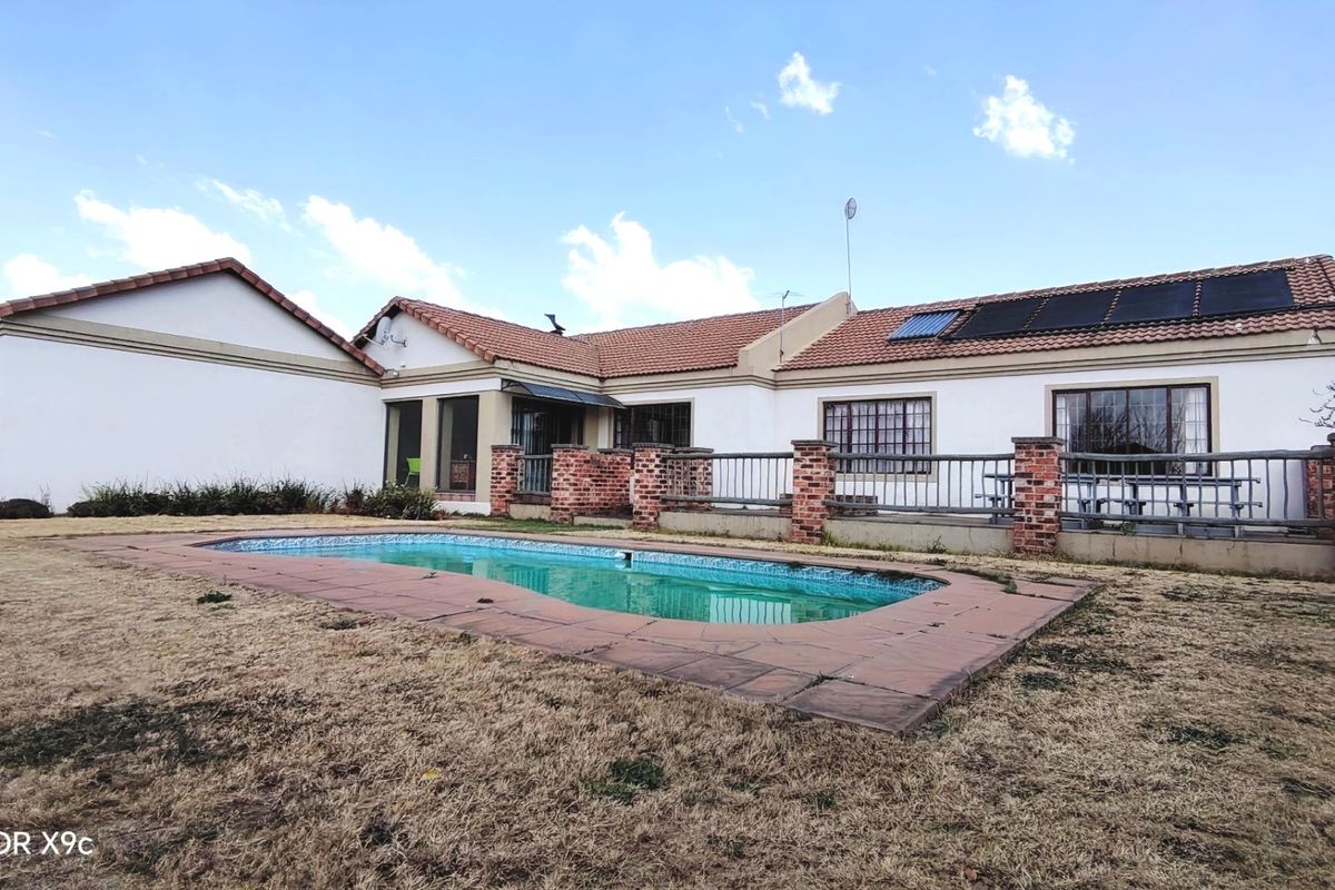 Rear view of the farm property featuring a swimming pool, paved surround, and solar water heating panels installed on the tiled roof.