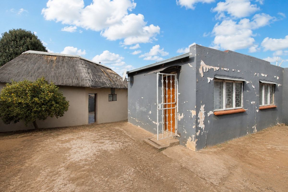 Rear view of the property featuring a traditional thatched structure and a secondary building with significant exterior paint deterioration and weathered plaster finishes.