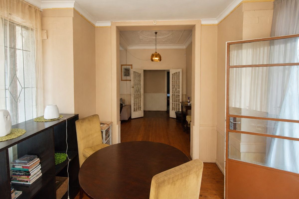 A living area featuring original timber flooring, decorative ceiling detailing, wainscoting, and classic french doors leading to an adjoining room.