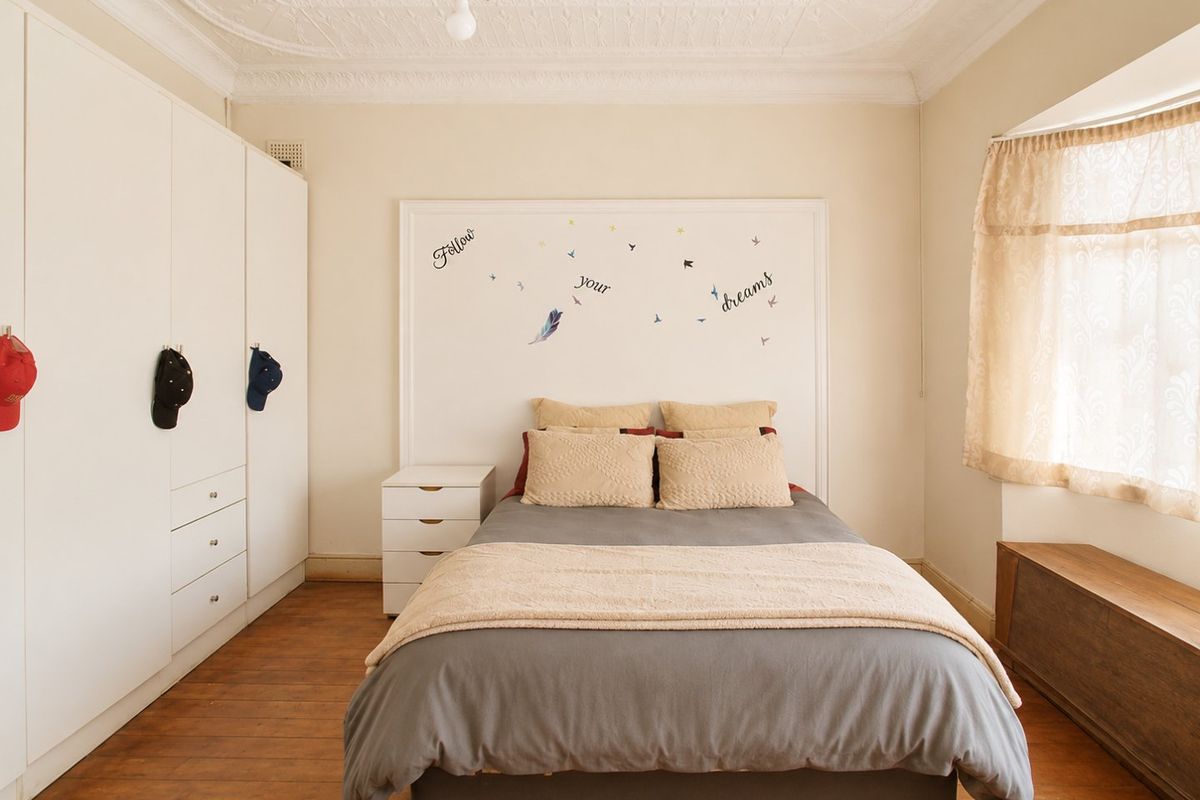 A well-proportioned bedroom featuring timber flooring, built-in cabinetry, and decorative ceiling detailing, offering a comfortable and functional living space.