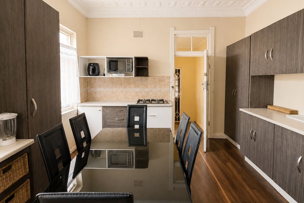 A functional kitchen featuring dark wood-look cabinetry, a gas cooktop, tiled splashback, and classic pressed metal ceilings, complemented by warm timber flooring.