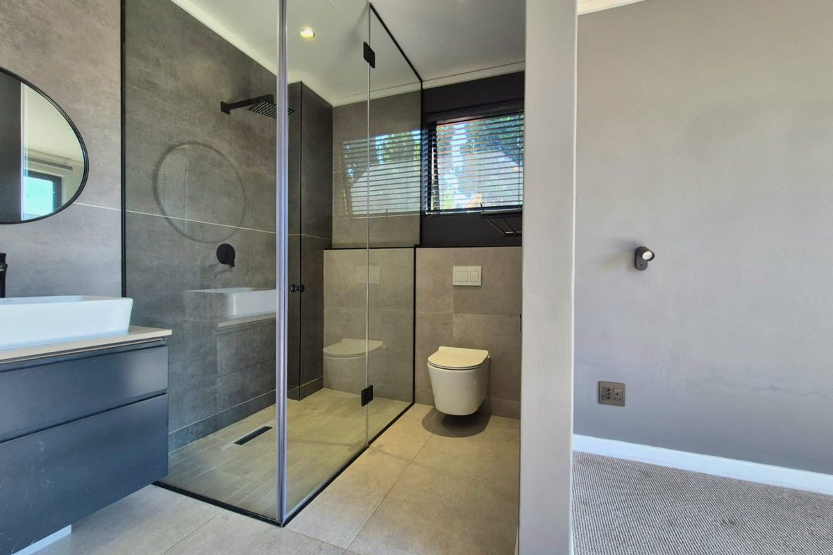 Modern bathroom featuring a walk-in shower with glass screen, wall-hung toilet, and a sleek vanity with vessel sink, finished with contemporary grey tiling.