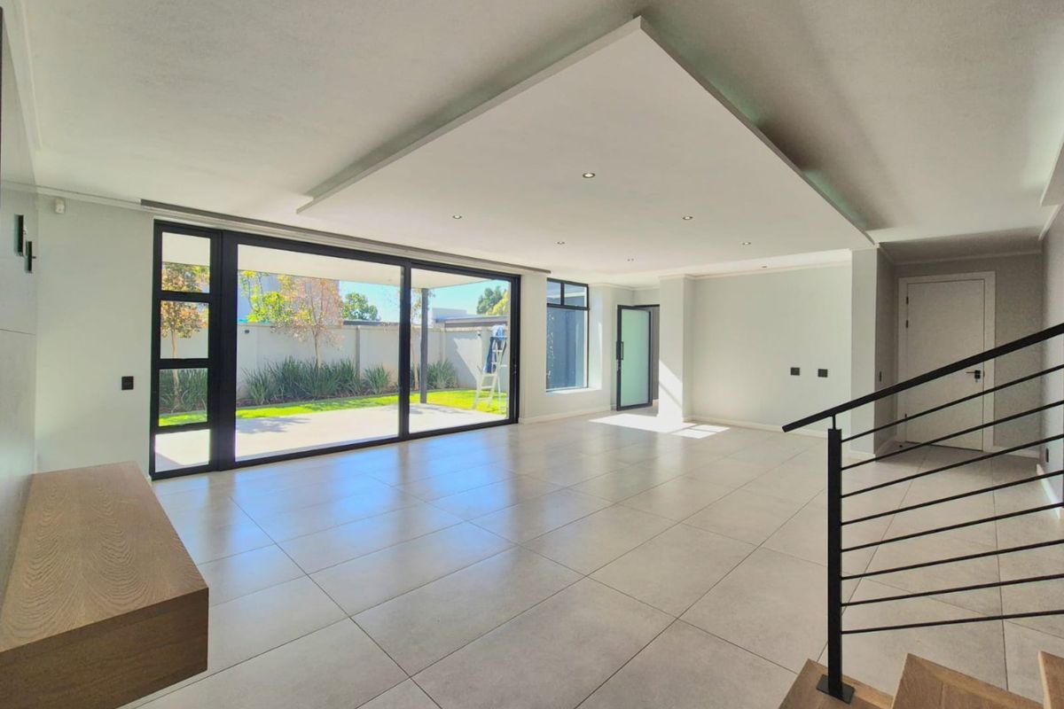 Spacious, modern open-plan living area featuring large format floor tiles, recessed ceiling lighting, and expansive sliding glass doors leading to the rear garden.