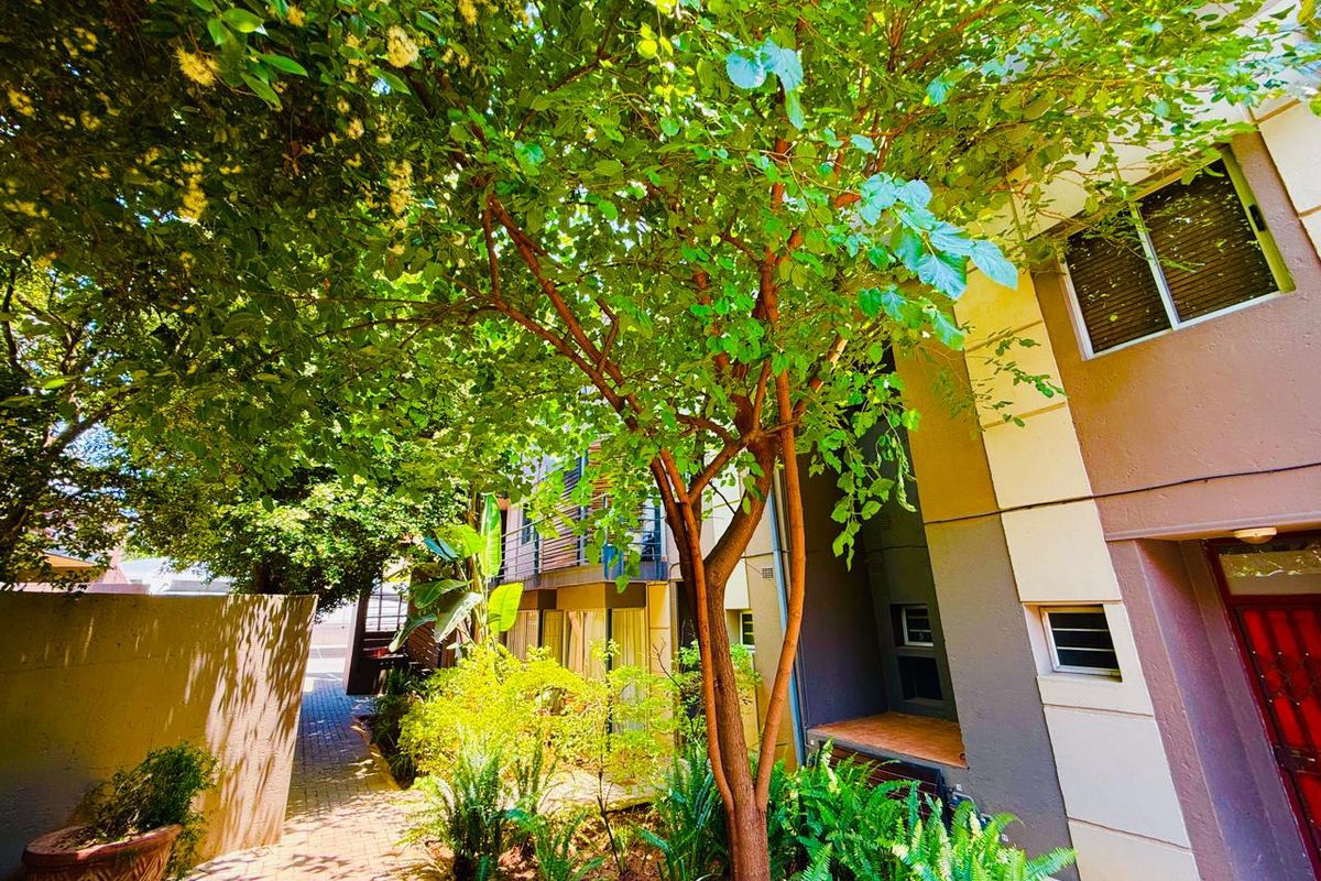 A view of the rear exterior area featuring a paved walkway, lush garden landscaping, and access to the building's entrance.