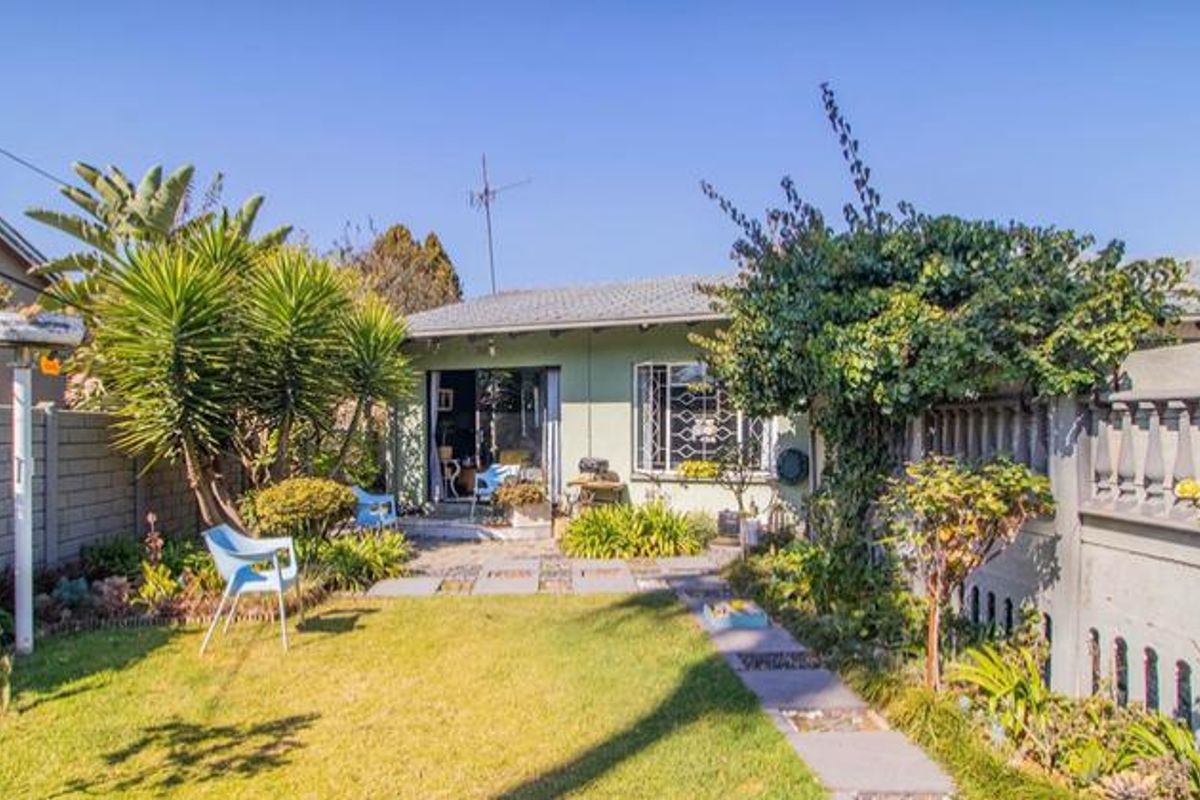 Rear view of the property featuring a private garden, paved walkway, and secure sliding door access to the main living area.