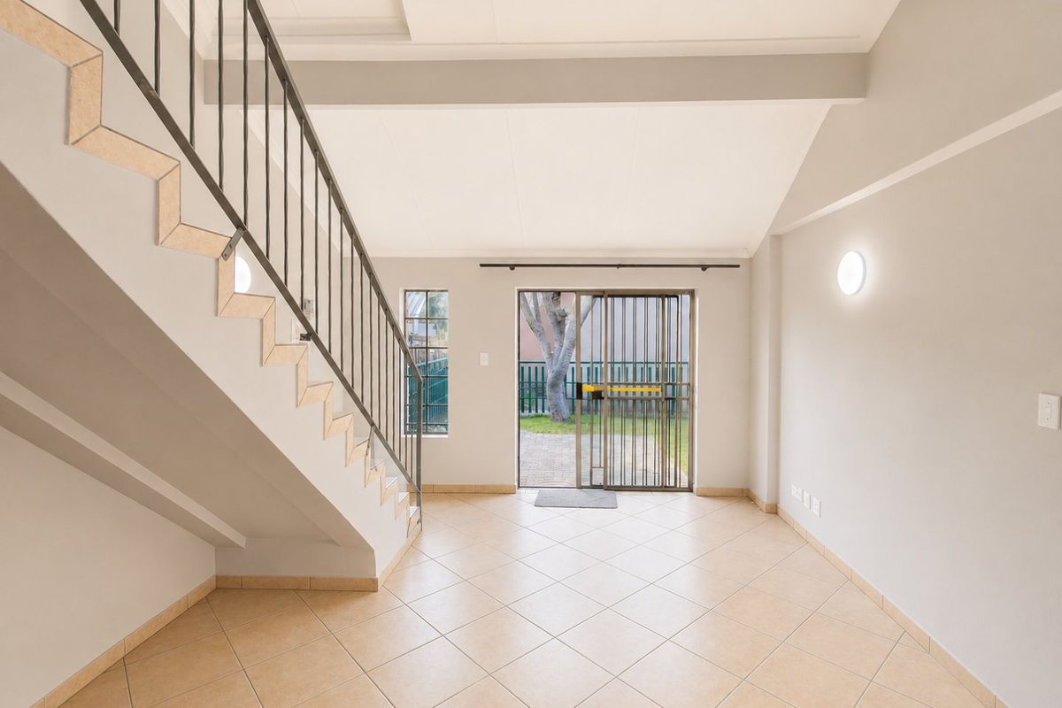 An open-plan living area featuring tiled flooring, a staircase with a metal balustrade, and a sliding glass door providing access to the rear garden.