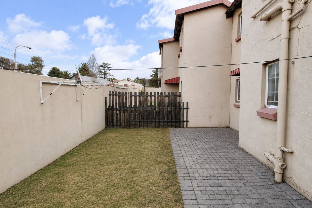 Rear exterior view of the townhouse featuring a small paved patio area, a patch of lawn, and a boundary wall with a timber gate.
