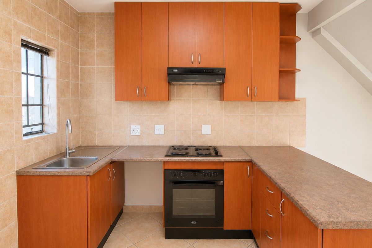 A functional kitchen featuring wood-look cabinetry, laminate countertops, a built-in oven with gas hob, and tiled finishes throughout.