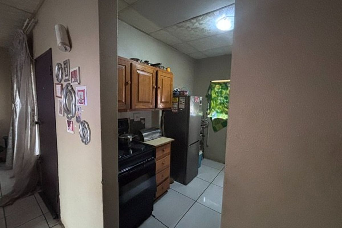 A compact kitchen featuring wooden cabinetry, tiled flooring, and a drop ceiling, offering a functional layout with potential for modern updates.