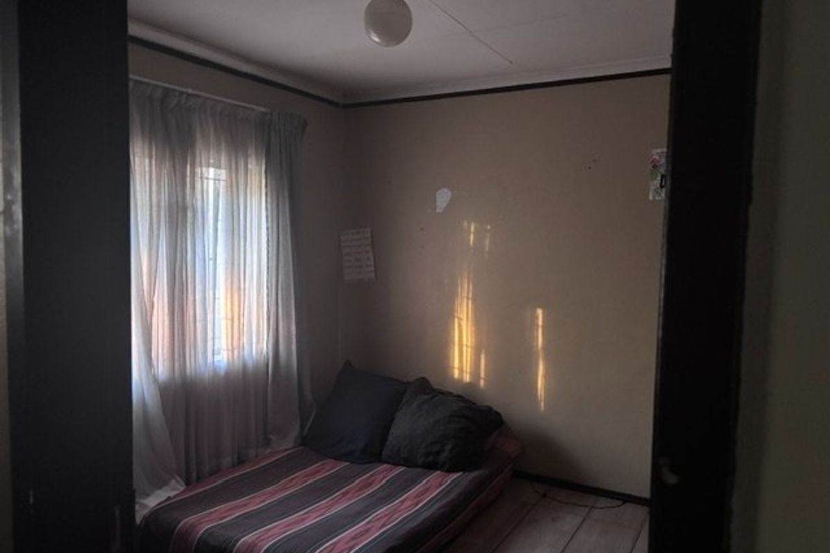 A compact bedroom featuring tiled flooring and natural light from a window, requiring cosmetic updates to improve its overall condition and appeal.