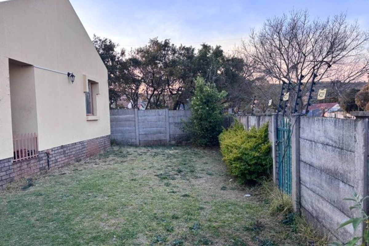 A rear garden area featuring a lawn, precast concrete boundary walls with electric fencing, and a metal pedestrian gate.
