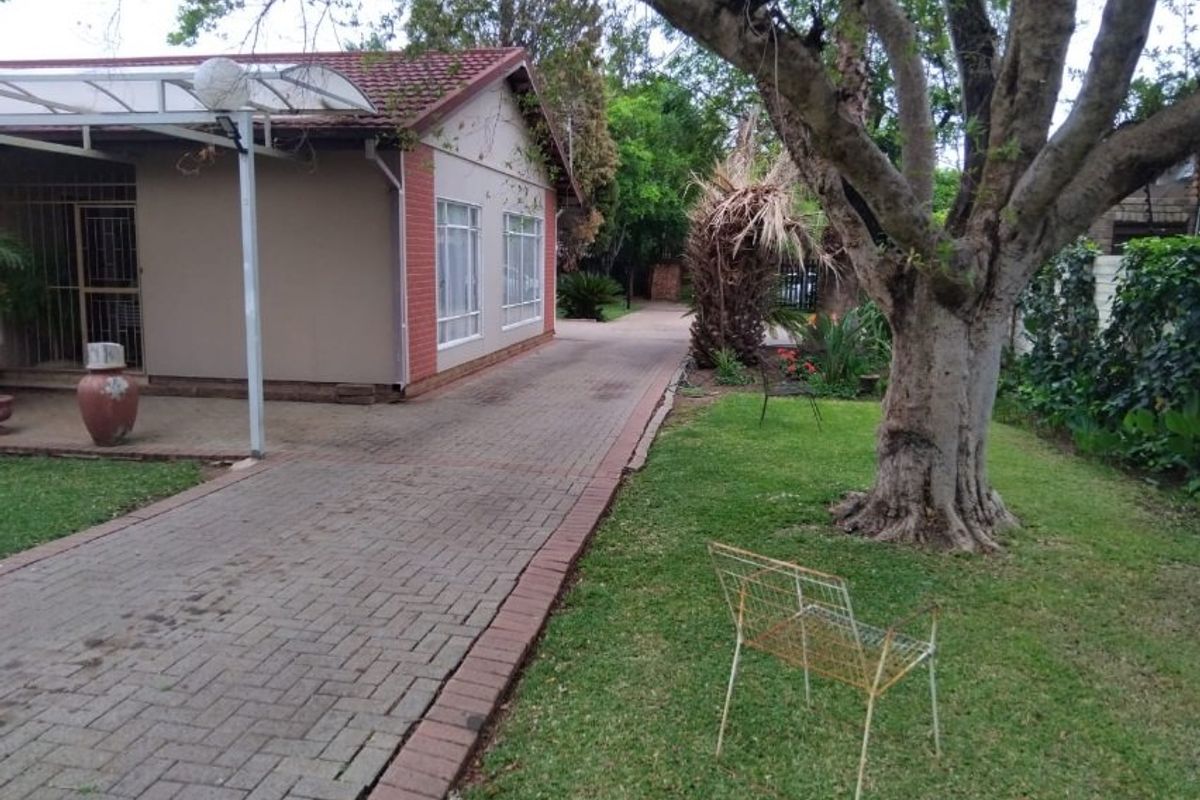 Rear view of the property featuring a paved driveway, covered patio area, and established garden space.